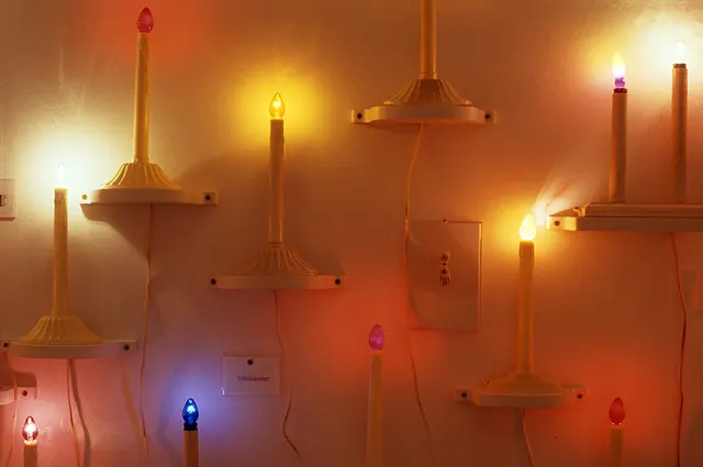 Surveying Desire VIII: Reconnaissance: detail view of candle wall with framed texts and objects of fortune